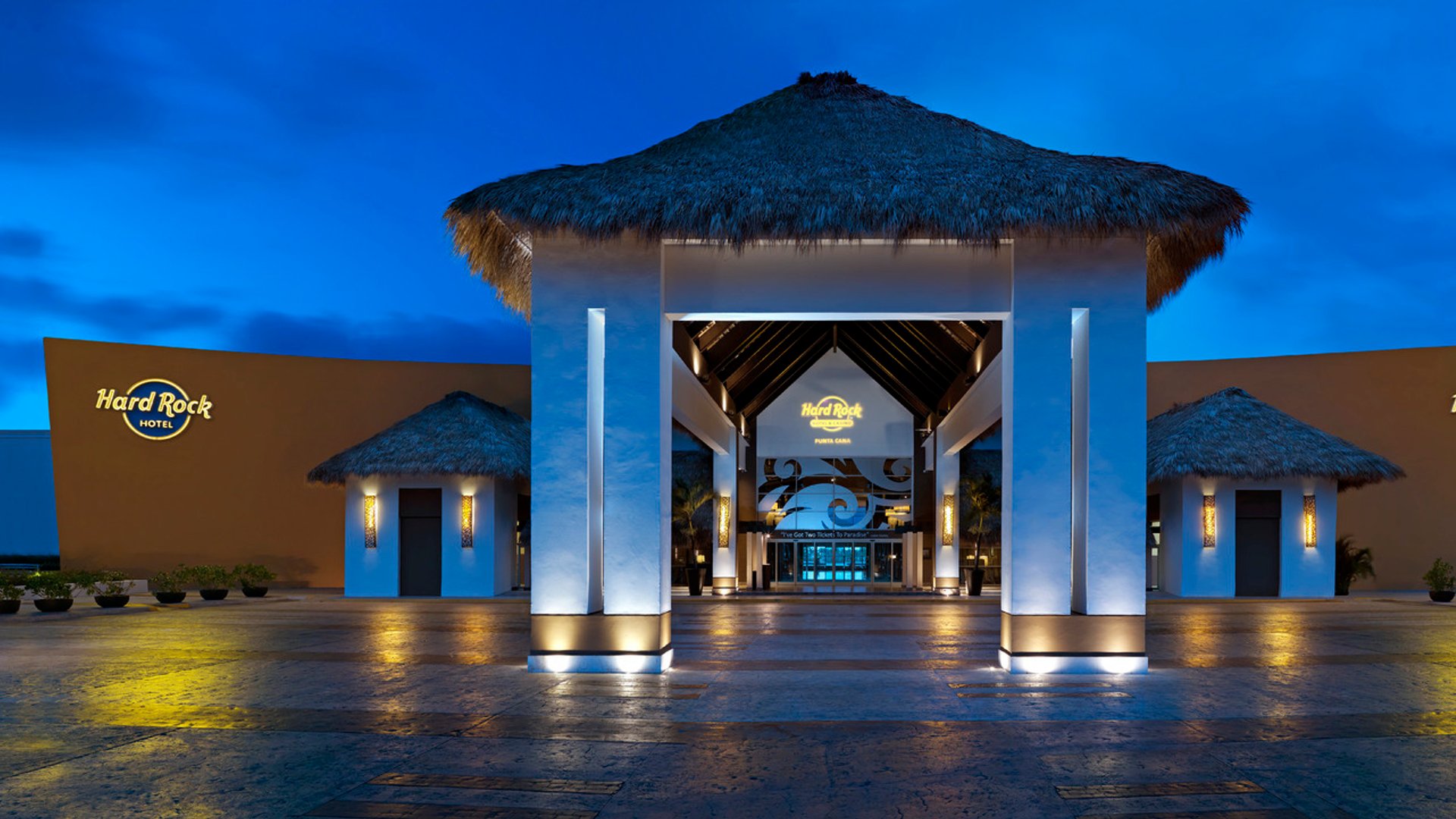 HRH Punta Cana main lobby entrance with thatched roof and illuminated pillars at dusk.