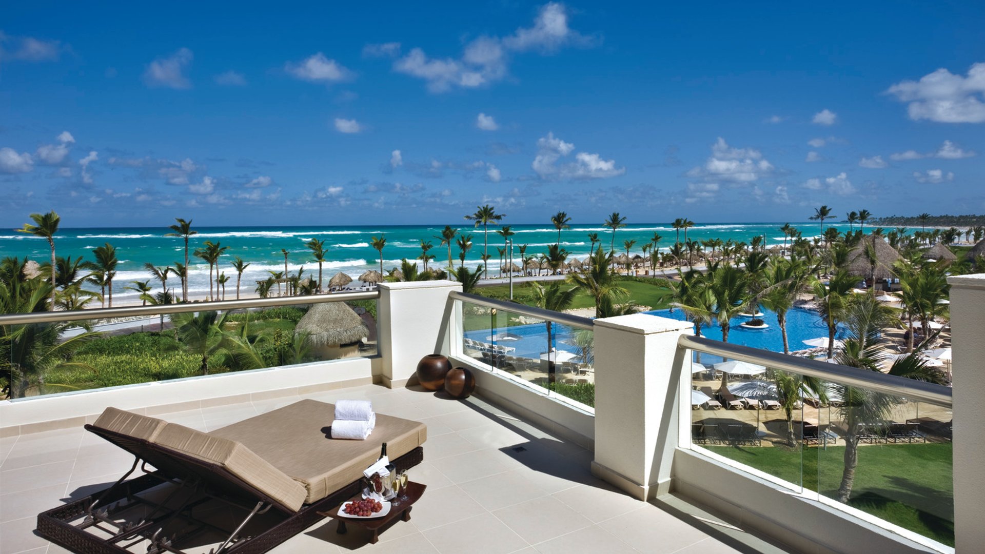 Balcony view of Punta Cana beach with chaise lounge, ocean, palm trees, and resort pool under a clear blue sky.